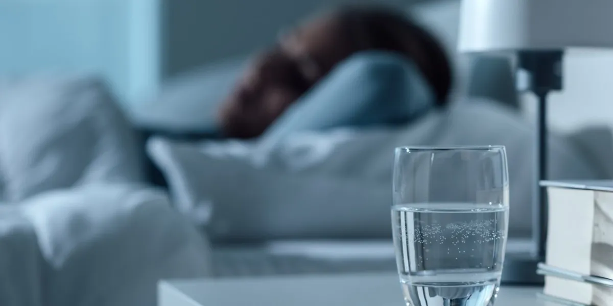 woman sleeping in her bed at night, glass on water and pills on the foreground, medicine and treatment concept