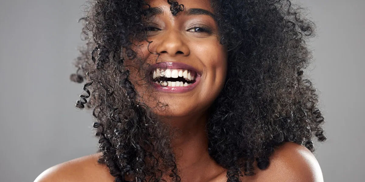 face, hair care and beauty smile of black woman on gray studio background portrait, makeup and female model from jamaica with beautiful, healthy head of hair and curls after spa cosmetics treatment
