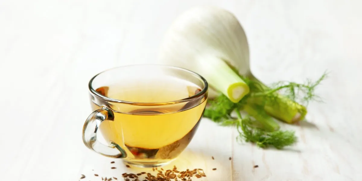 fennel tea in a glass bowl, fresh fennel on a white wooden background