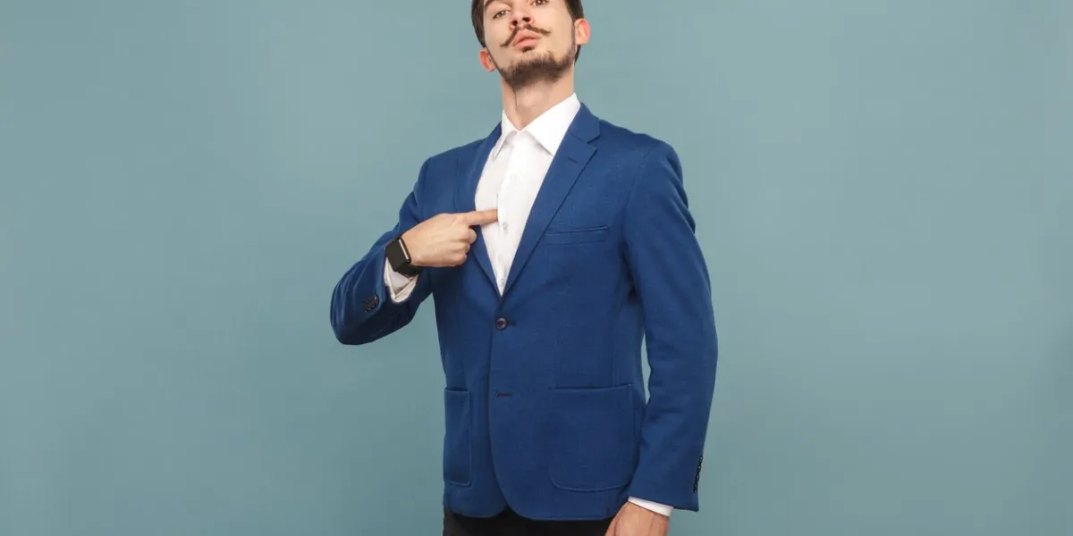 proud man pointing finger himself portrait of handsome bearded businessman in blue suit and white shirt, with smart watch indoor studio shot, isolated on light blue background