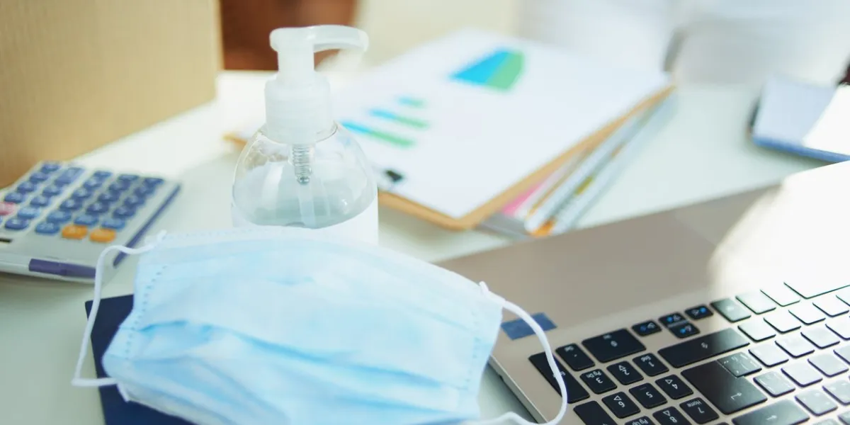 closeup on medical mask and hand disinfectant on the table in temporary home office during the coronavirus epidemic in the living room in sunny day