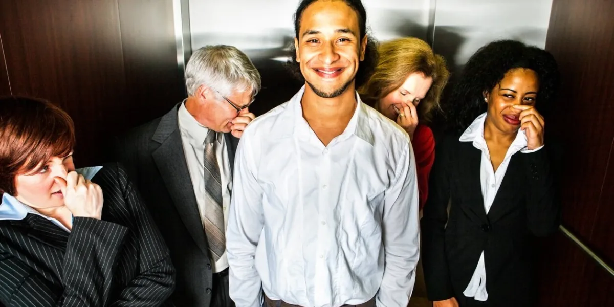 a young man smiles in embarrassment (or pride) in an elevator while people hold their noses