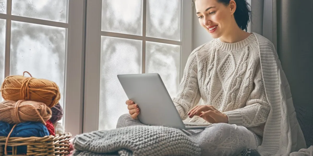 happy beautiful woman watching videos or enjoying entertainment content on a laptop sitting near windows in the house in the winter