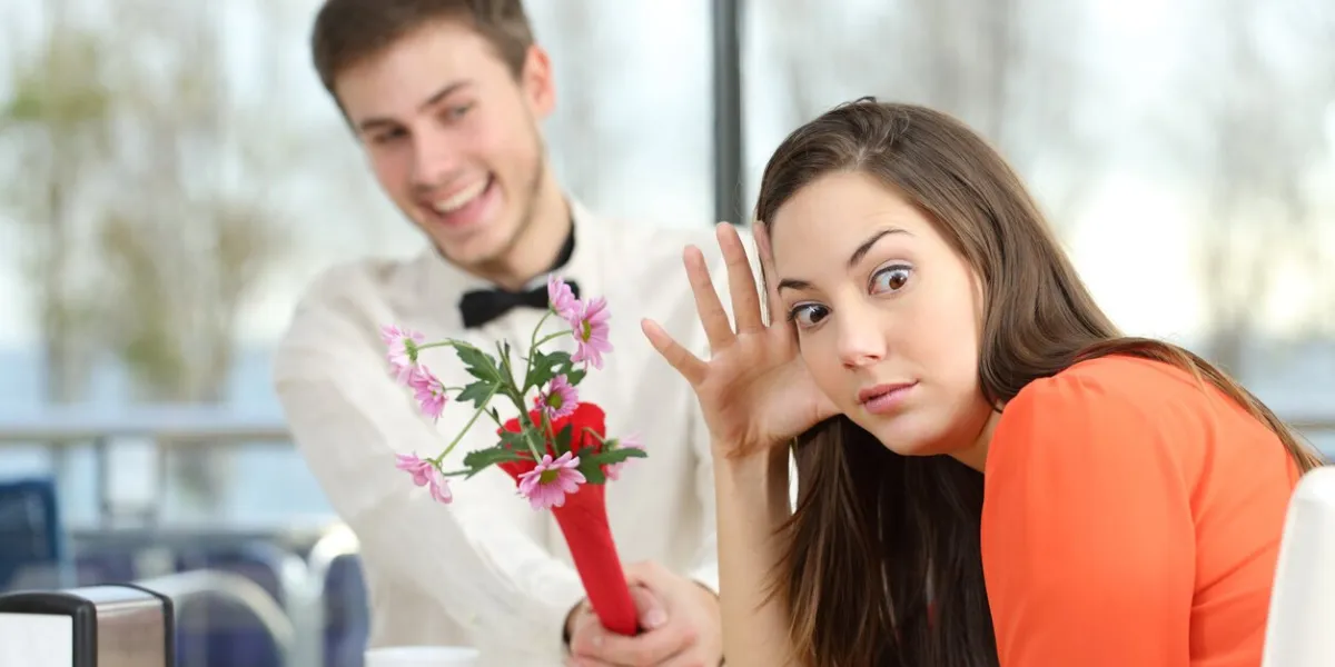 disgusted woman rejecting a geek boy offering flowers in a blind date in a coffee shop interior