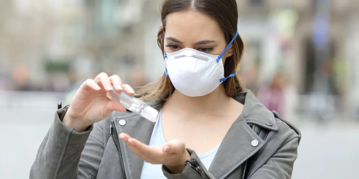 portrait of a serious girl wearing protective mask applying sanitizer hand rub preventing contagion on city street