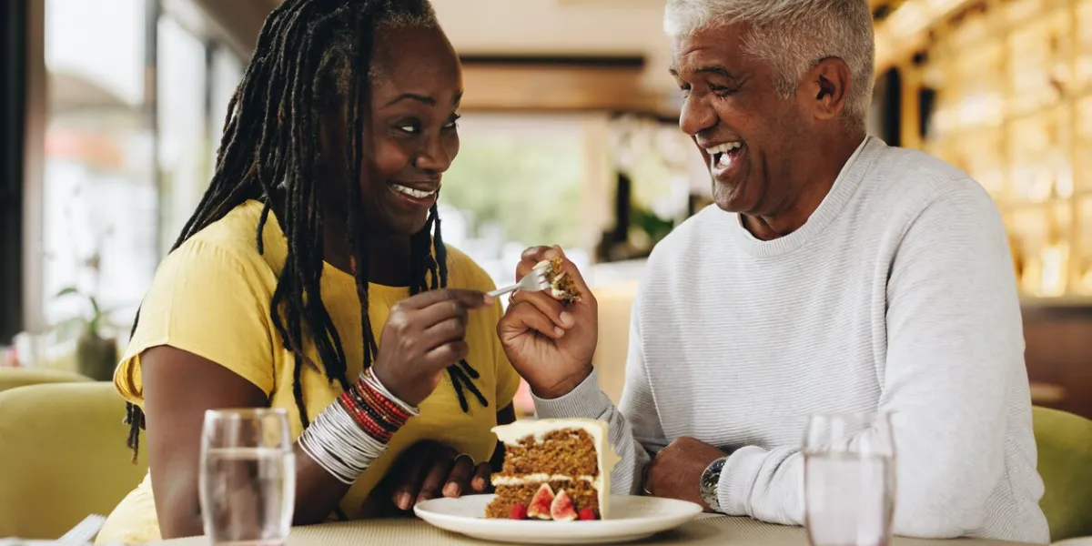 senior couple smiling at each other while sharing a delicious cake in a cafe happy senior couple having a good time in a restaurant cheerful mature couple enjoying their retirement together