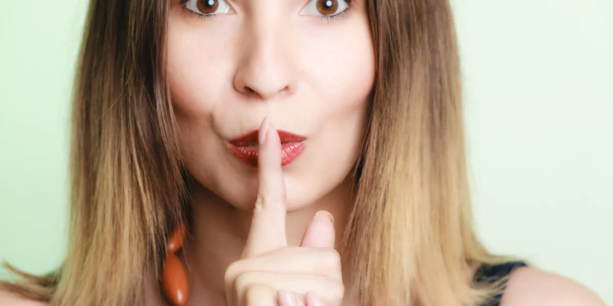 portrait de jeune femme fille demandant le silence ou le secret avec le doigt sur les lèvres chut main geste sur le vert