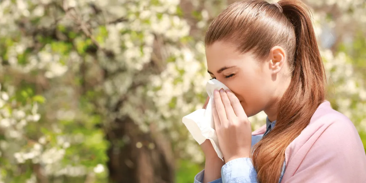 sneezing young girl with nose wiper among blooming trees in park