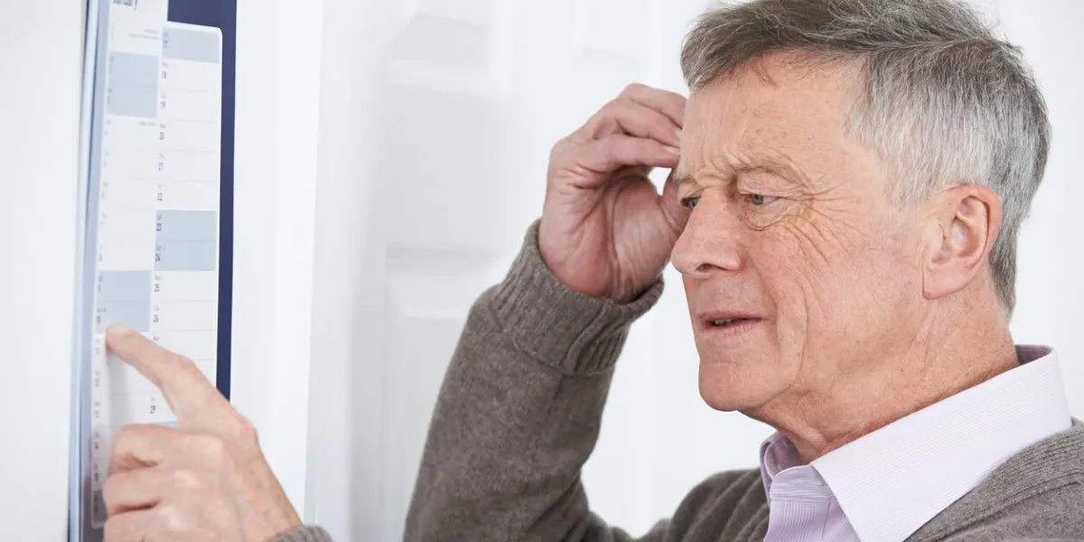 confused senior man with dementia looking at wall calendar