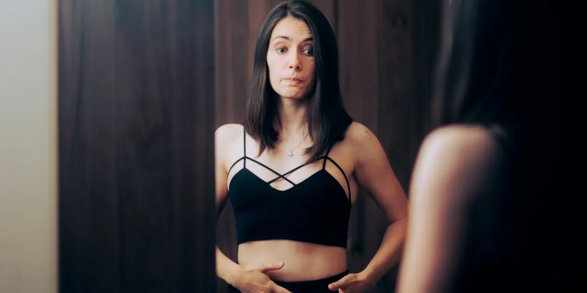 girl feeling bloated looking at her stomach in mirror reflection