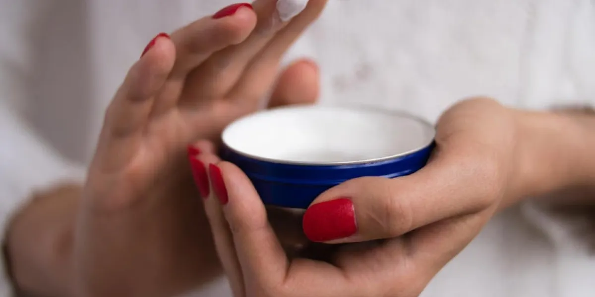mains féminines avec des ongles rouges appliqué la crème sur le pot bleu