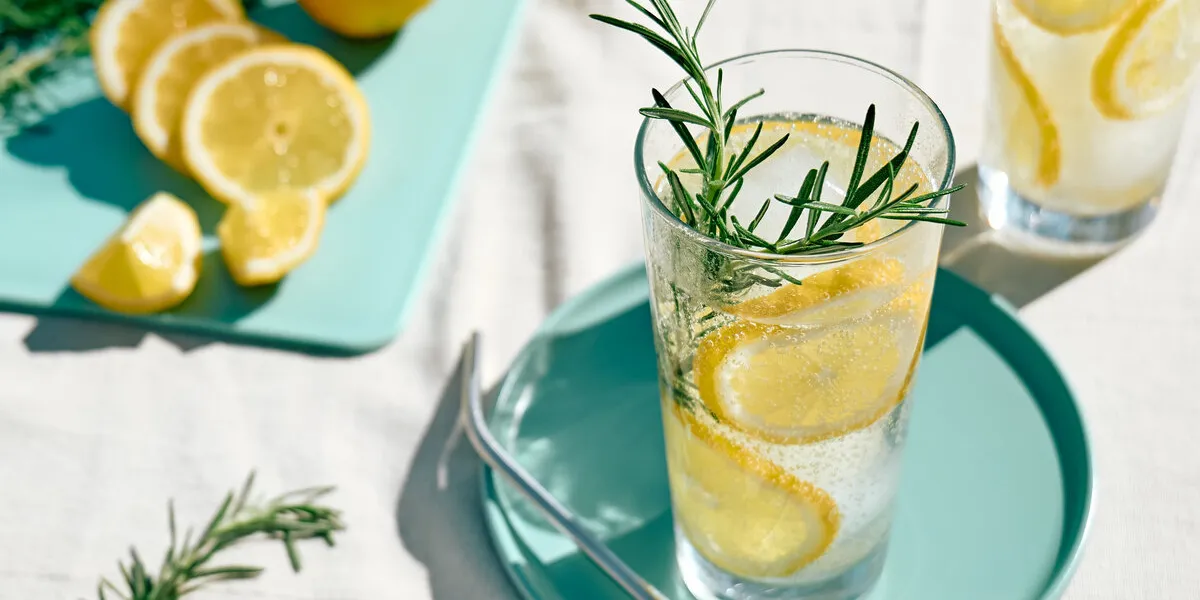 summer refreshing lemonade drink or alcoholic cocktail with ice, rosemary and lemon slices on the table in the garden fresh healthy cold lemon beverage water with lemon