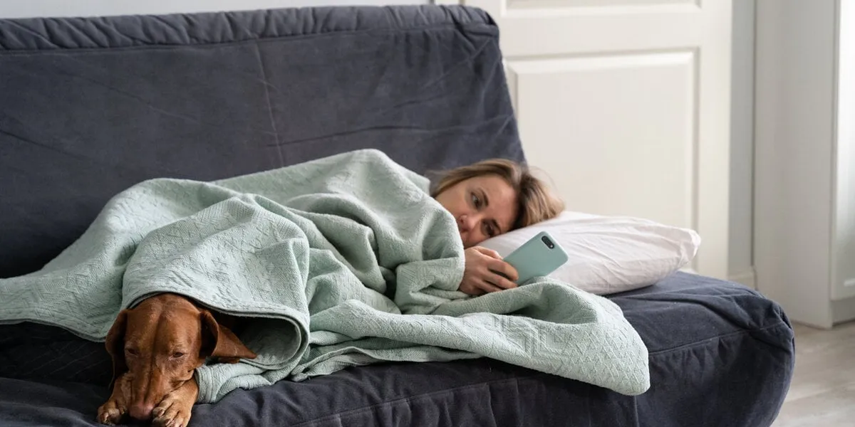 sad woman lying on sofa with dog, using smart phone in hands wait for boyfriend call or text, feels depressed thoughtful female think about relationships problems mental health, loneliness concept