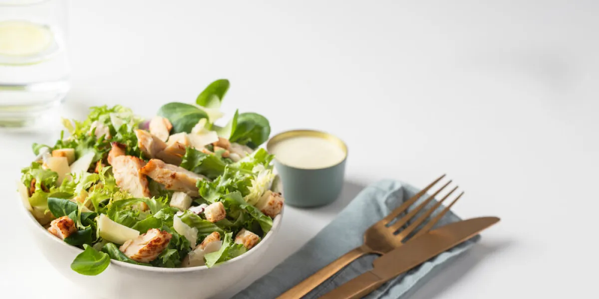 cesar salad plate served with water glass, sauce bowl and cutlery in restaurant table