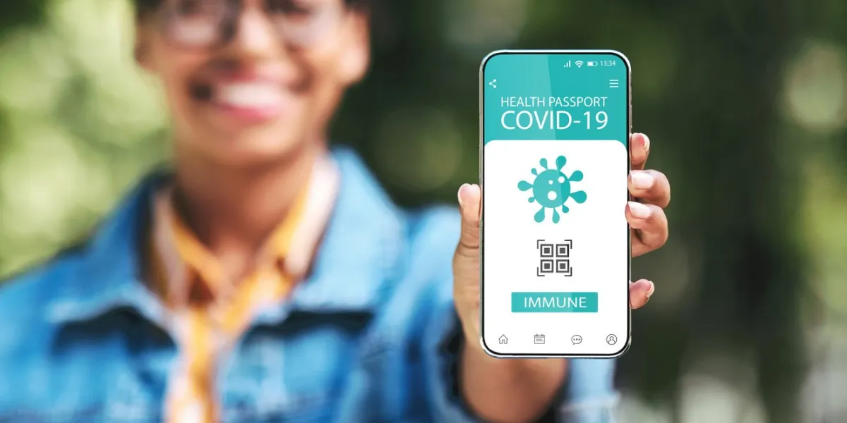 ready for travel smiling black young woman holding cellphone with digital health e-passport in hand, showing mobile application and confirming that she has immunity for covid-19, selective focus