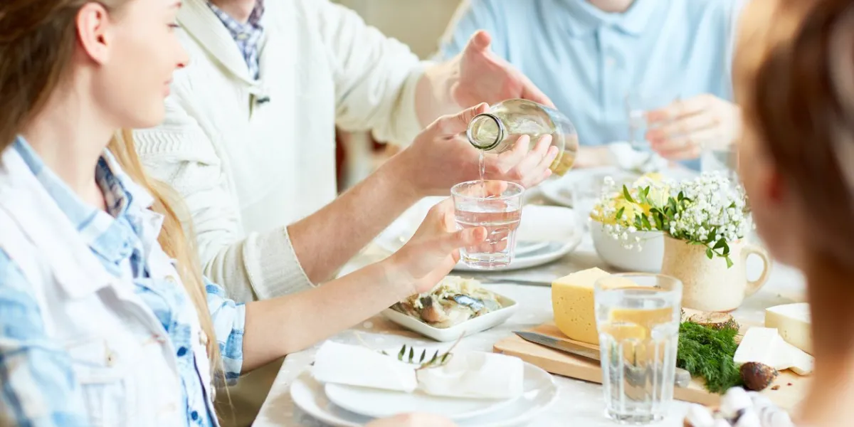 young man pouring homemade lemonade in glass of his girlfriend while having dinner with friends
