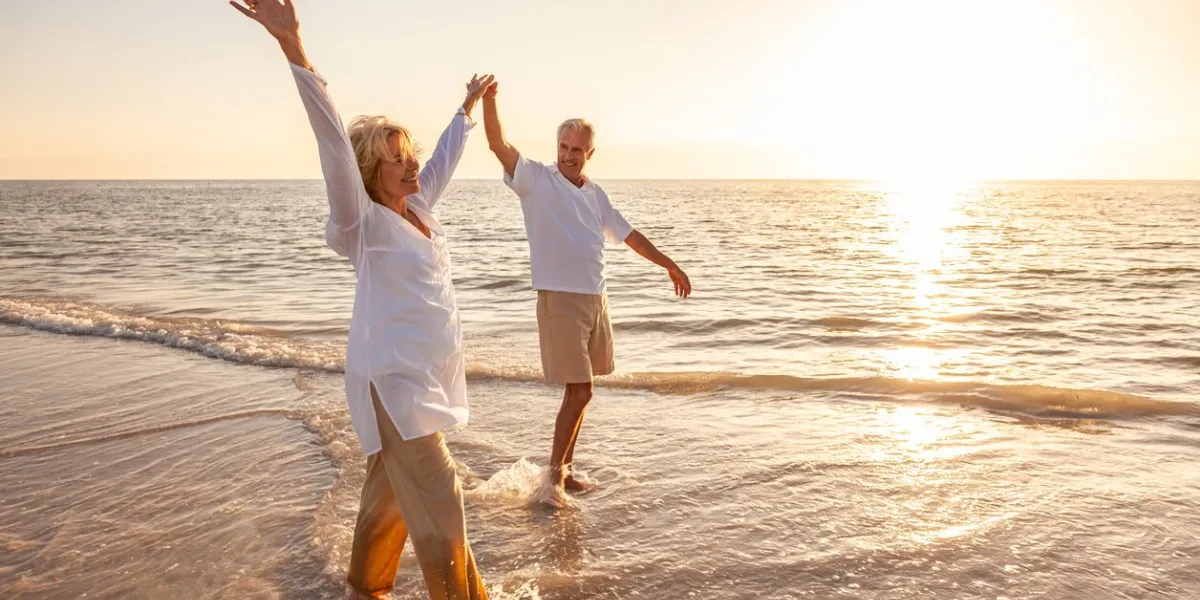 happy senior man and woman old retired couple walking and holding hands on a beach at sunset