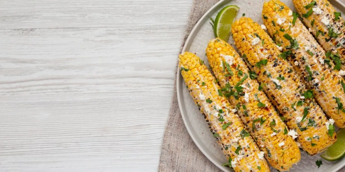 homemade elote mexican street corn on a plate on a white wooden background, top view flat lay, overhead, from above space for text