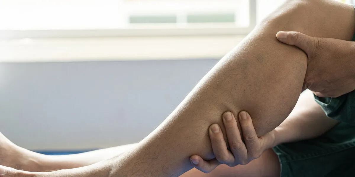 young man suffering from cramps lying on the bed by the window and suffering from leg cramps