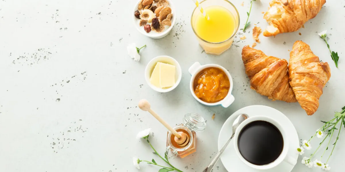continental breakfast captured from above (top view, flat lay) coffee, orange juice, croissants, jam, honey and flowers grey stone worktop as background layout with free text (copy) space