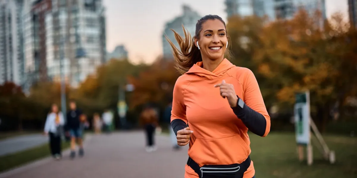 young happy athletic woman listening music on earphones while jogging in the park