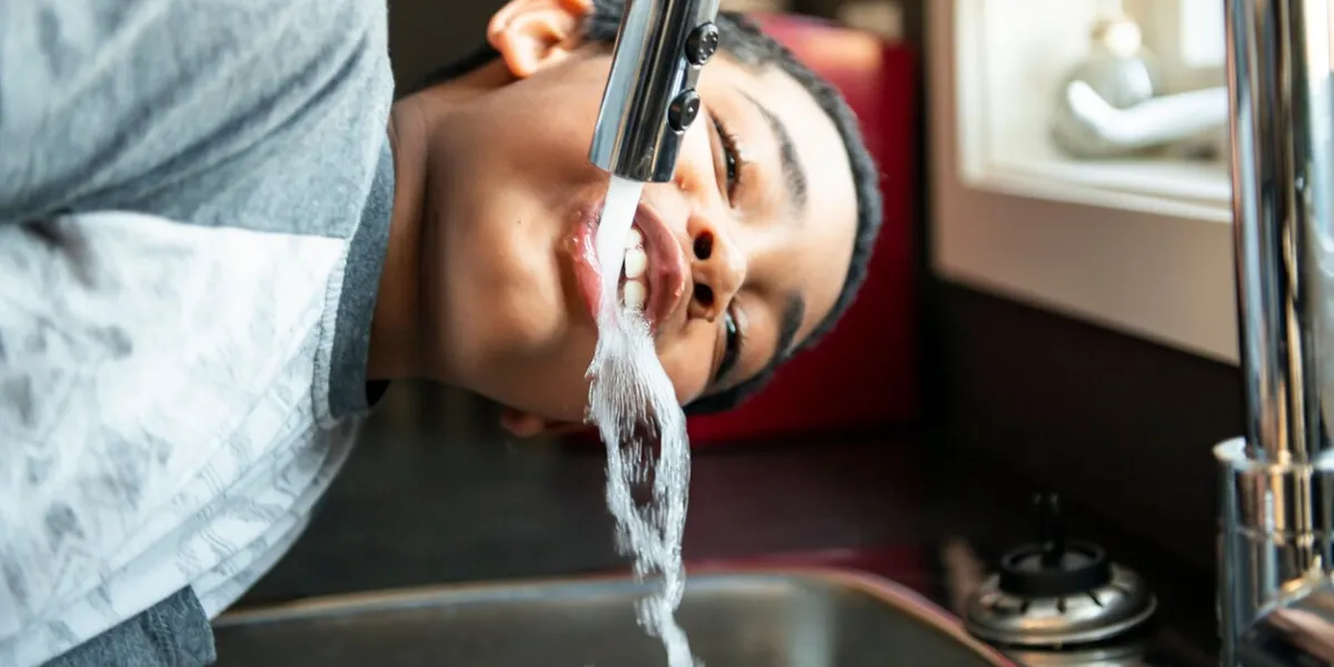 a child afro american boy take water on his mouth and drink in a kitchen