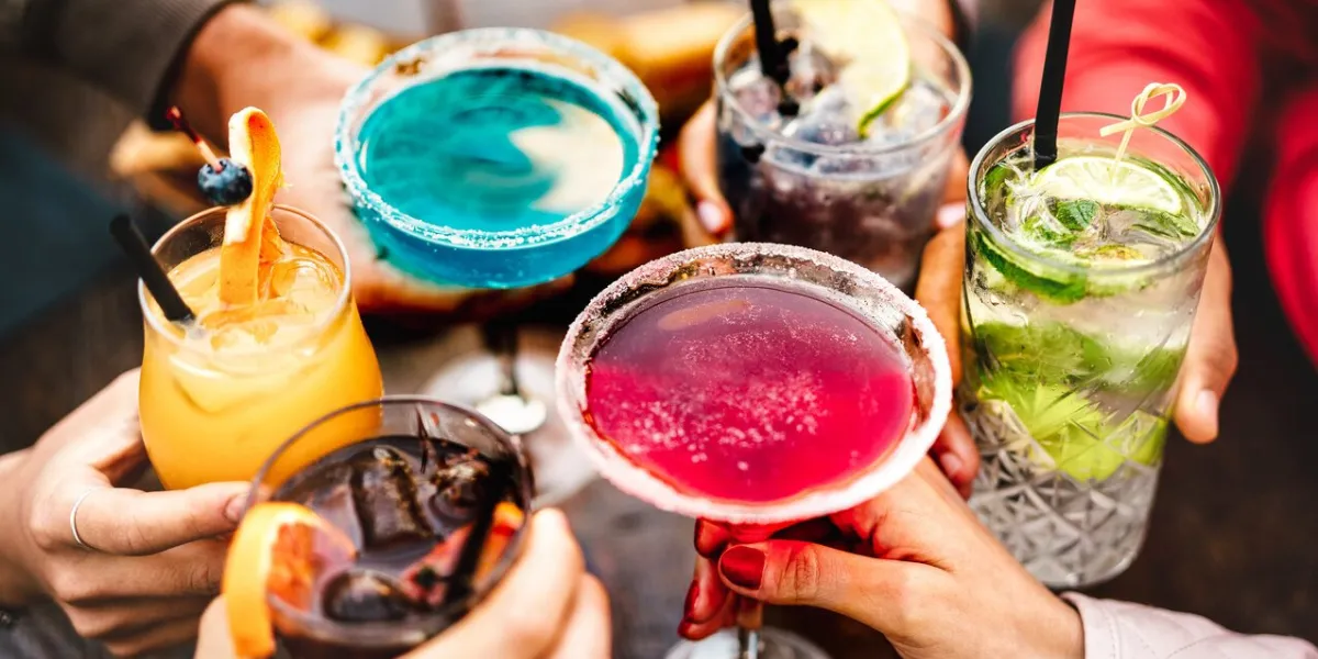 people hands toasting multicolored fancy drinks - young friends having fun together drinking cocktails at happy hour - social gathering party time concept on warm vivid filter