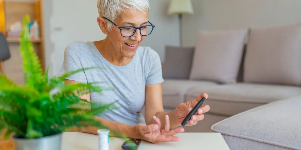 happy mature woman with glucometer checking blood sugar level at home woman testing for high blood sugar woman holding device for measuring blood sugar