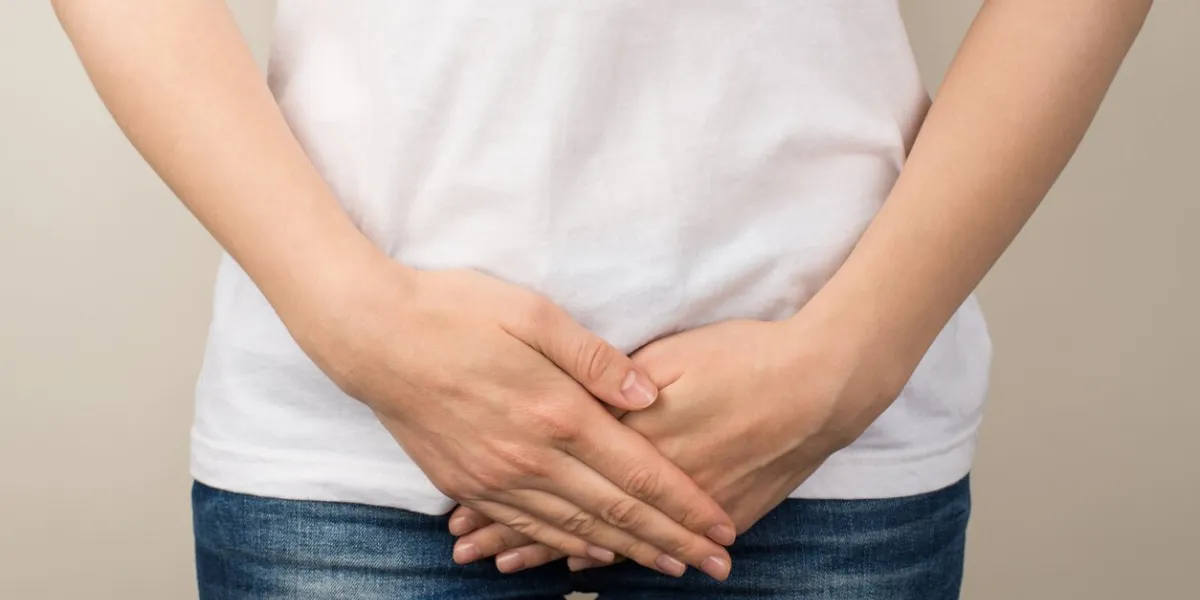 cropped closeup photo of young woman in white t-shirt and jeans holding her hands on crotch on isolated grey background