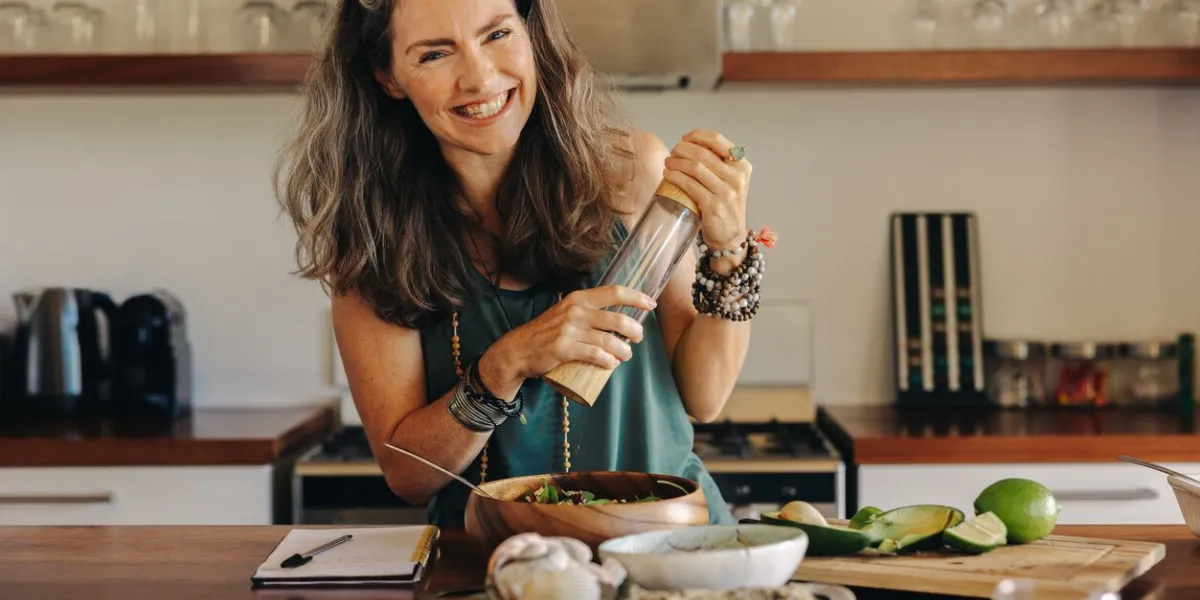 senior woman smiling at the camera while preparing some plant-based food cheerful woman following a healthy vegan recipe in her kitchen happy mature woman eating clean at home