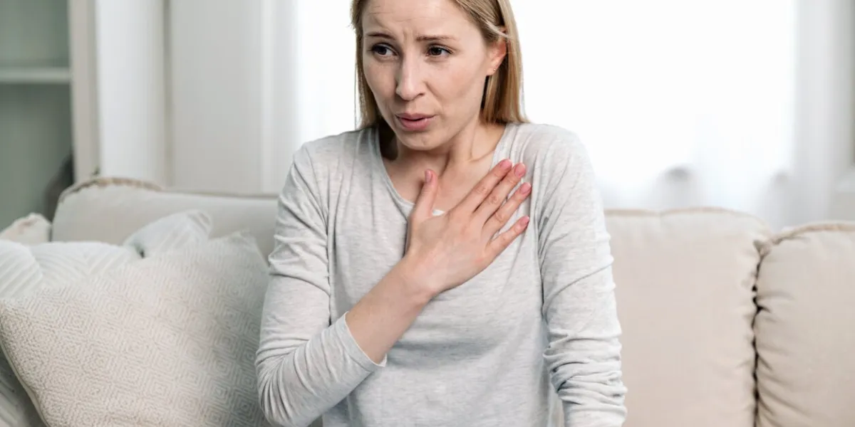 worried woman feeling acute cardiac pain, hold hand on chest and having difficulty breathing while sitting on couch at home young female have panic attack and afraid for her health