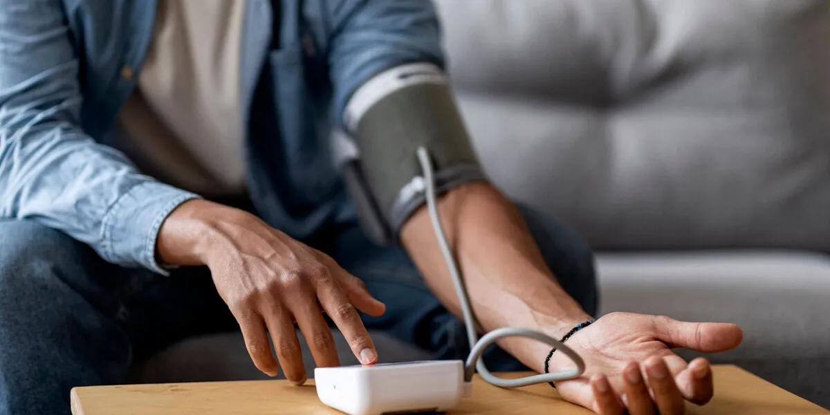 cropped shot of young black man checking blood pressure with upper arm monitor while sitting on couch at home, unrecognizable african american male measuring arterial tension, closeup