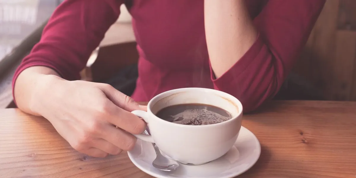 une jeune femme prend une tasse de café près de la fenêtre dans un café