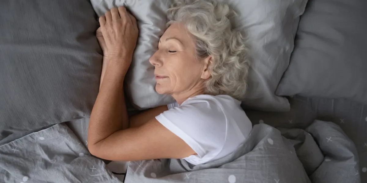 above top view calm peaceful elderly mature hoary woman sleeping on soft pillow under blanket, enjoying sweet dreams at night happy middle aged granny lying on side, resting in comfortable bed alone