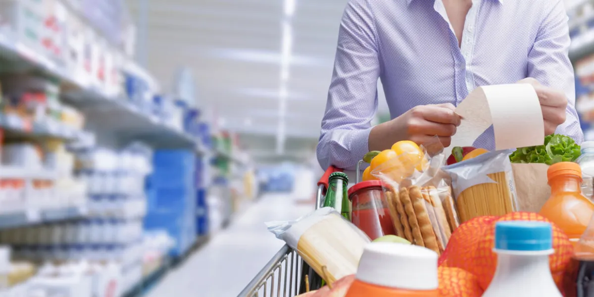 woman pushing a cart and checking a grocery receipt, grocery shopping and expenses concept