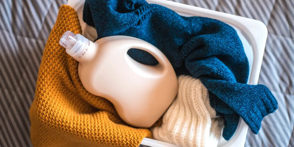 bottle of detergent with sweaters in container on the bed at home