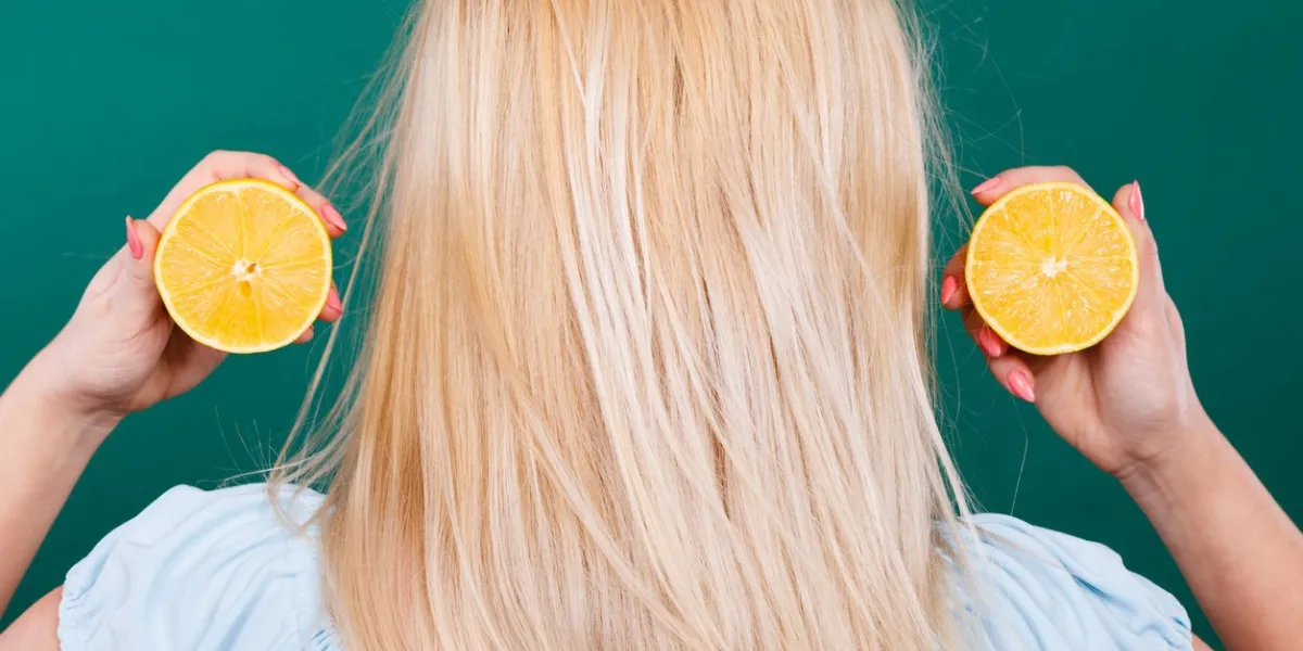 woman blonde girl holding two halfs of yellow lemon citrus fruit in hands, back view, on dark green healthy diet nutrition