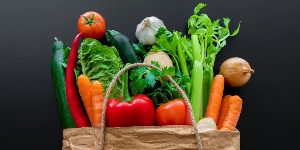 top view of fresh organic vegetables bought on weekly market in brown paper bag against dark table background