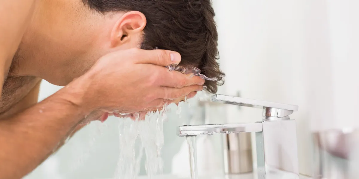 vue de côté d'un jeune homme torse nu, laver le visage dans la salle de bain