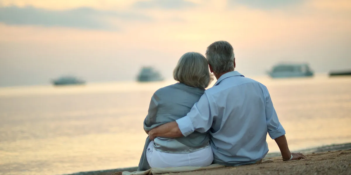 portrait of happy mature couple relaxing on beach at sunset