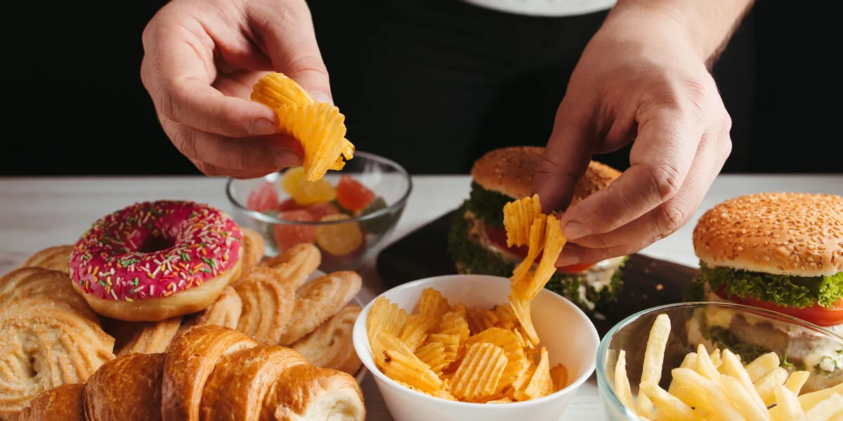 unhealthy snack, junk food, compulsive overeating man overeating unhealthy meals taking hamburger and potato chips from plate