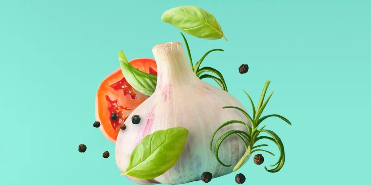 garlic falling in air with pepper and herbs like rosemary and basil leaves on turquoise background spicy food concept