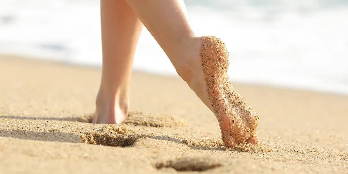 woman legs and feet walking on the sand of the beach with the sea water in the background