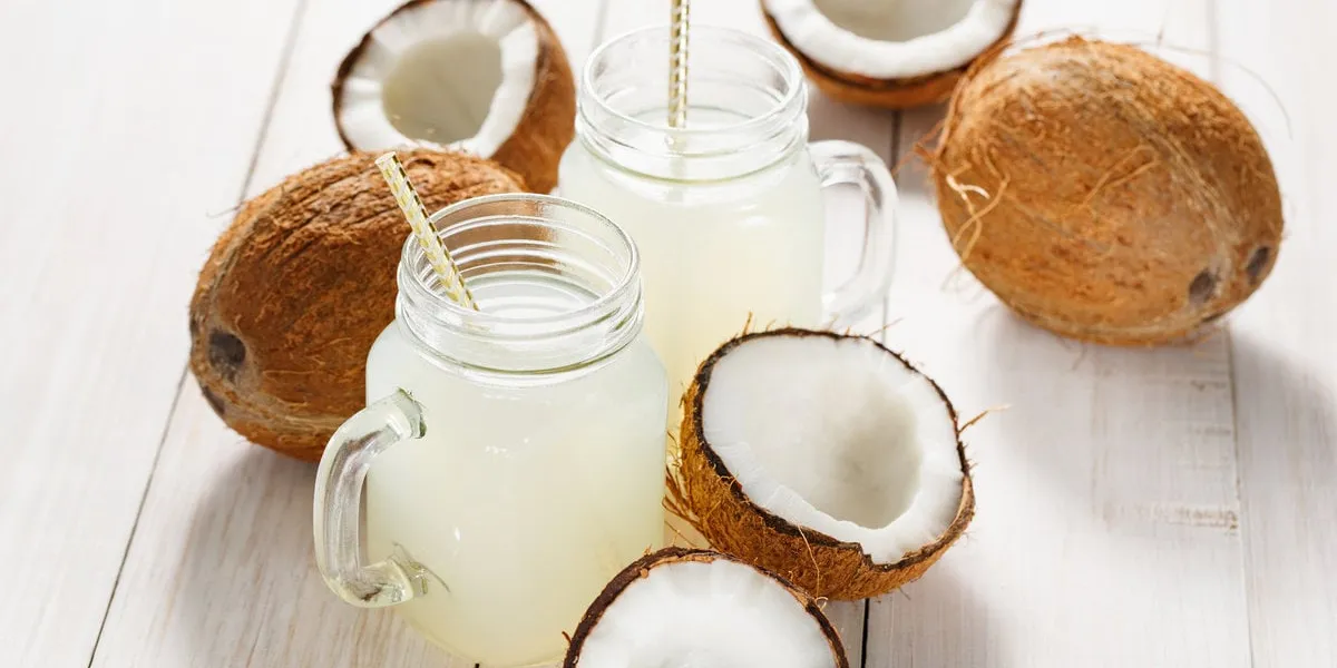 refreshing coconut water in jars and coconuts on a wooden white background
