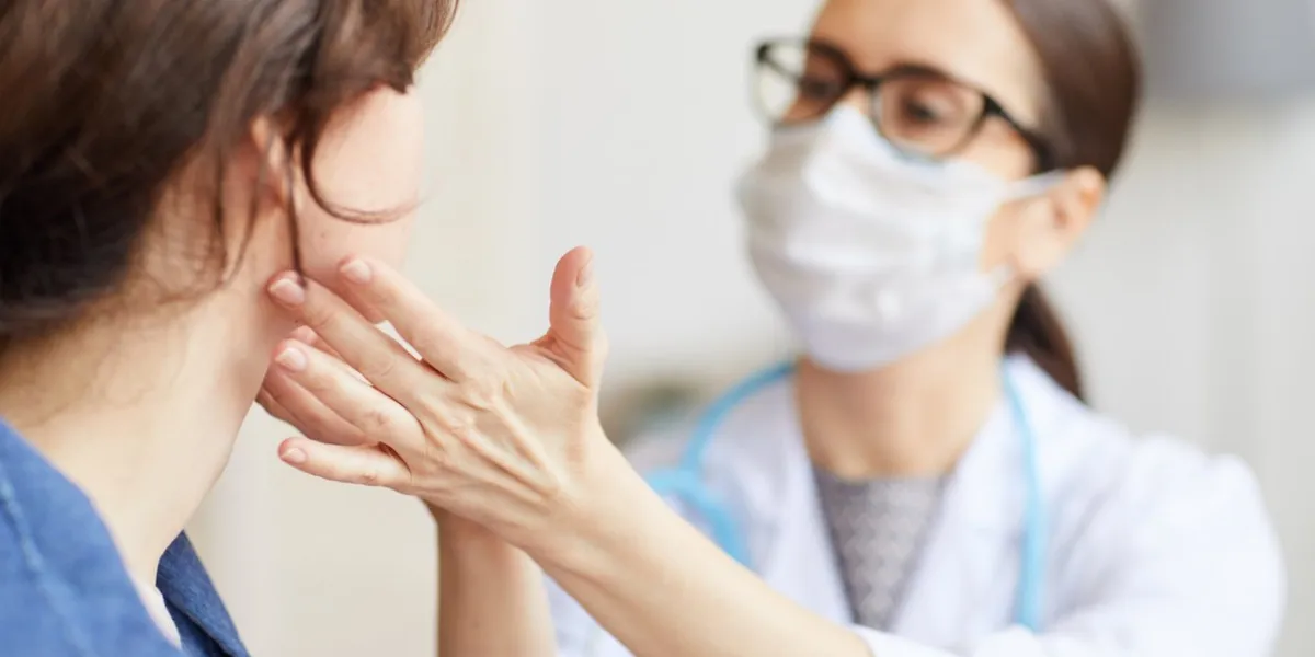 young woman sitting while the nurse examining her throat during visit at hospital