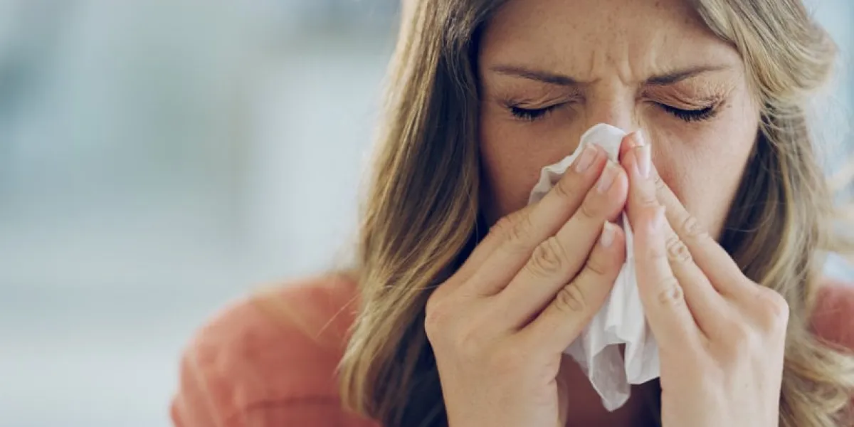 shot of an attractive young woman feeling ill and blowing her nose with a tissue at home