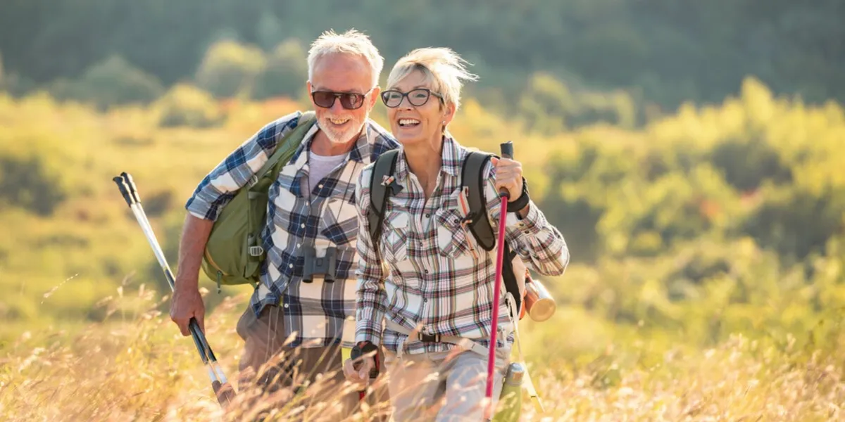 active senior caucasian couple hiking in mountains with backpacks and hiking poles, enjoying their adventure