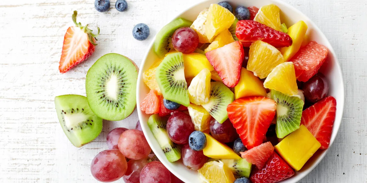 bowl of healthy fresh fruit salad on wooden background top view