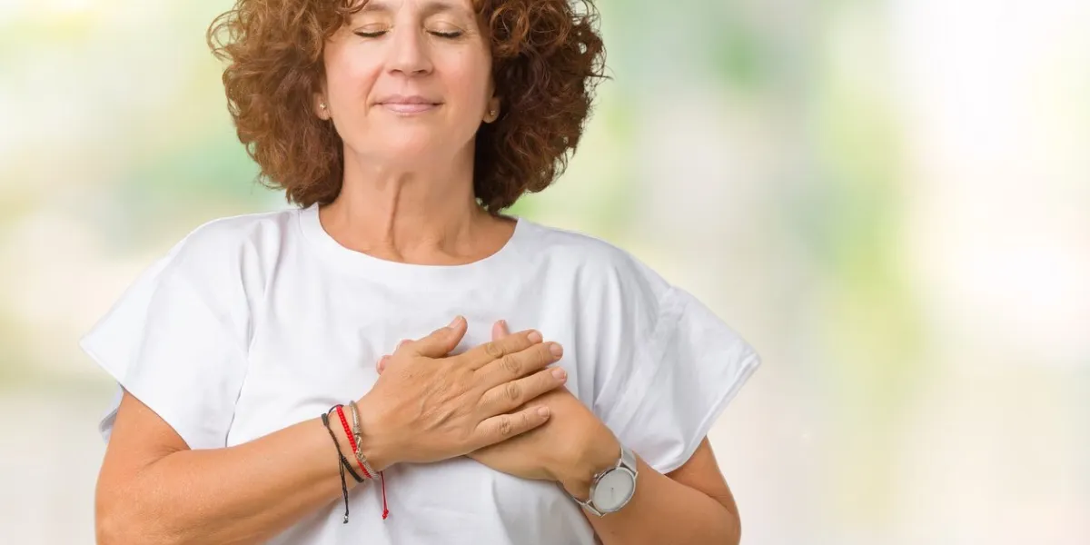 beautiful middle ager senior woman wearing white t-shirt over isolated background smiling with hands on chest with closed eyes and grateful gesture on face health concept