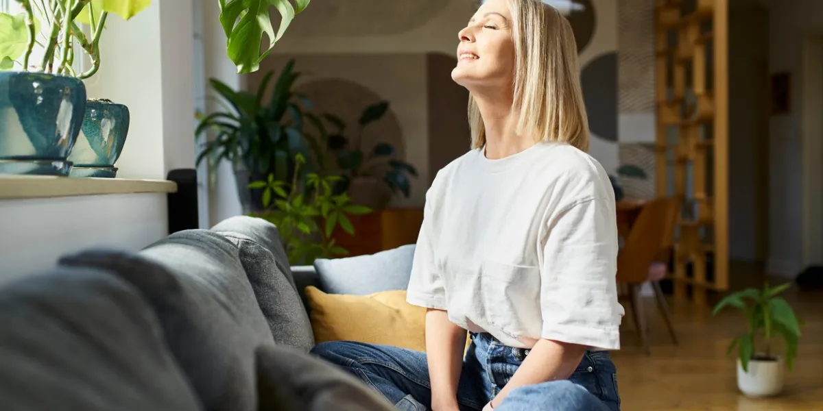 happy adult woman sitting on the sofa with eyes closed enjoying bright daylight